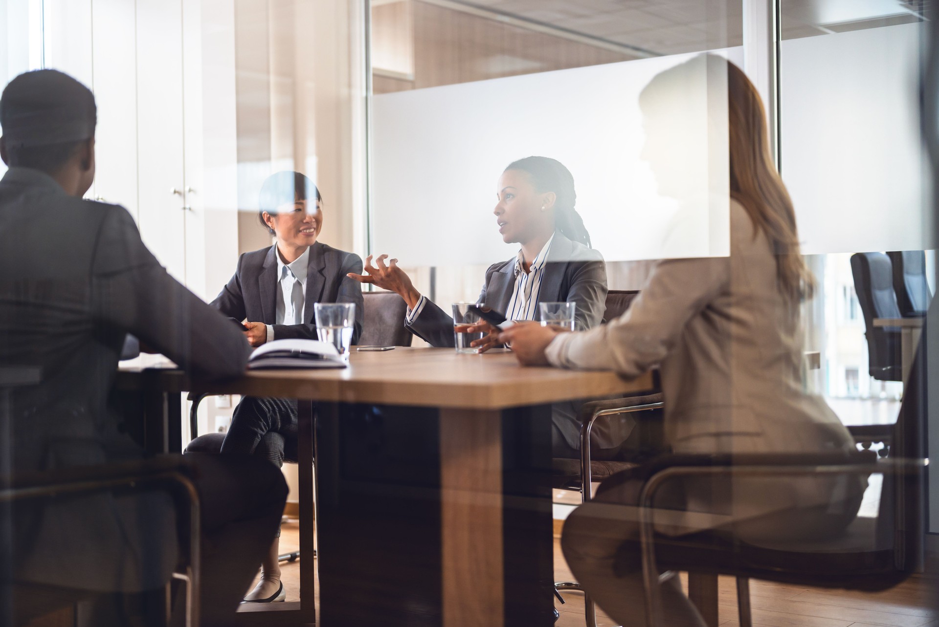 In a corporate office, a diverse group of multi-ethnic businesswomen and businessmen gather for a meeting. Cheerful participants engage in lively discussions and dialogue